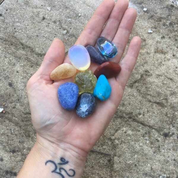 A hand holding 8 different coloured crystals